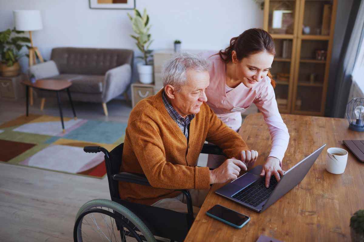 Donna che aiuta anziano disabile ad utilizzare il computer