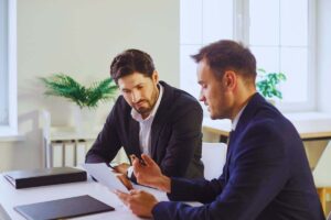 Uomini in abiti eleganti che esaminano documento mentre sono seduti alla scrivania