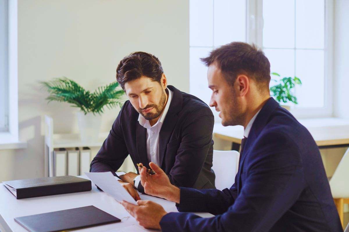 Uomini in abiti eleganti che esaminano documento mentre sono seduti alla scrivania