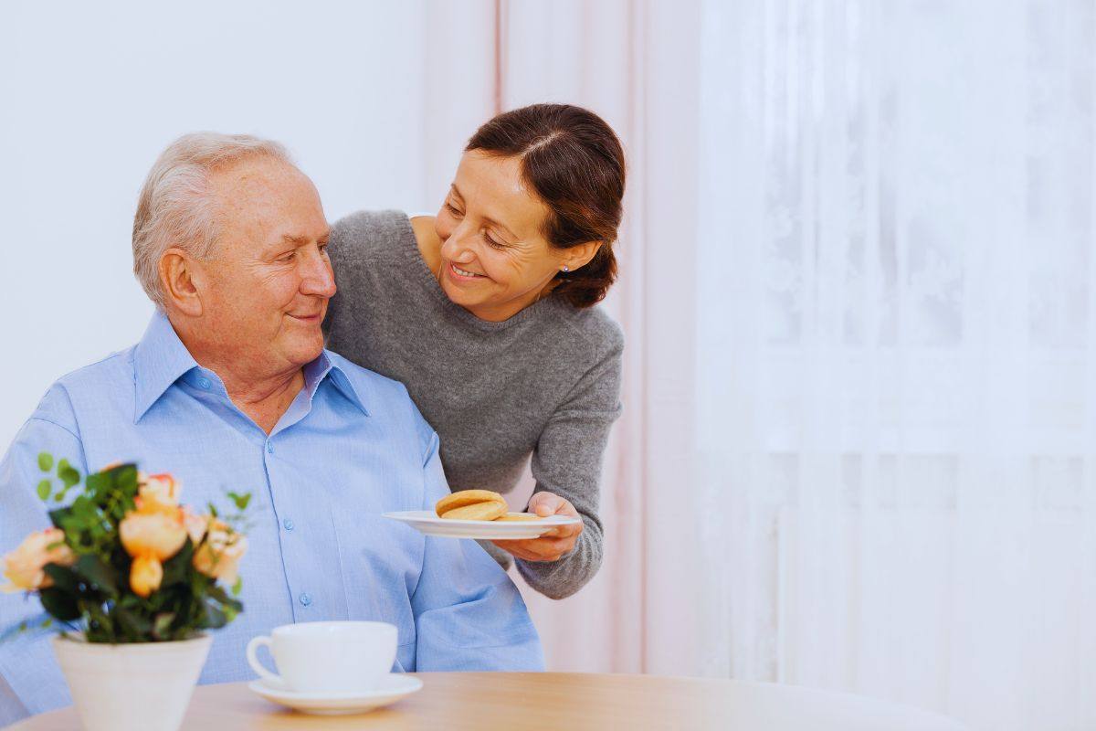 Donna che porta colazione ad anziano disabile