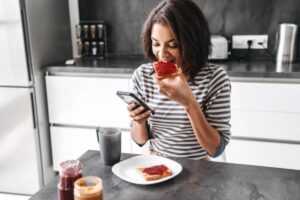 donna che mangia una fetta biscottata con marmellata mentre guarda il cellulare