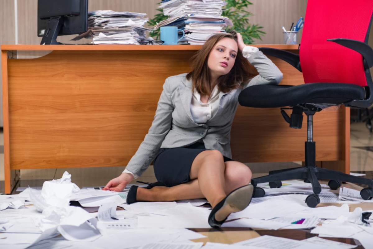 donna stressata seduta sul pavimento in ufficio circondata da fogli