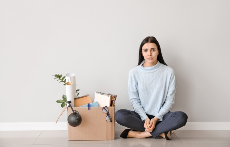 donna licenziata seduta per terra con accanto uno scatolone pieno di cose