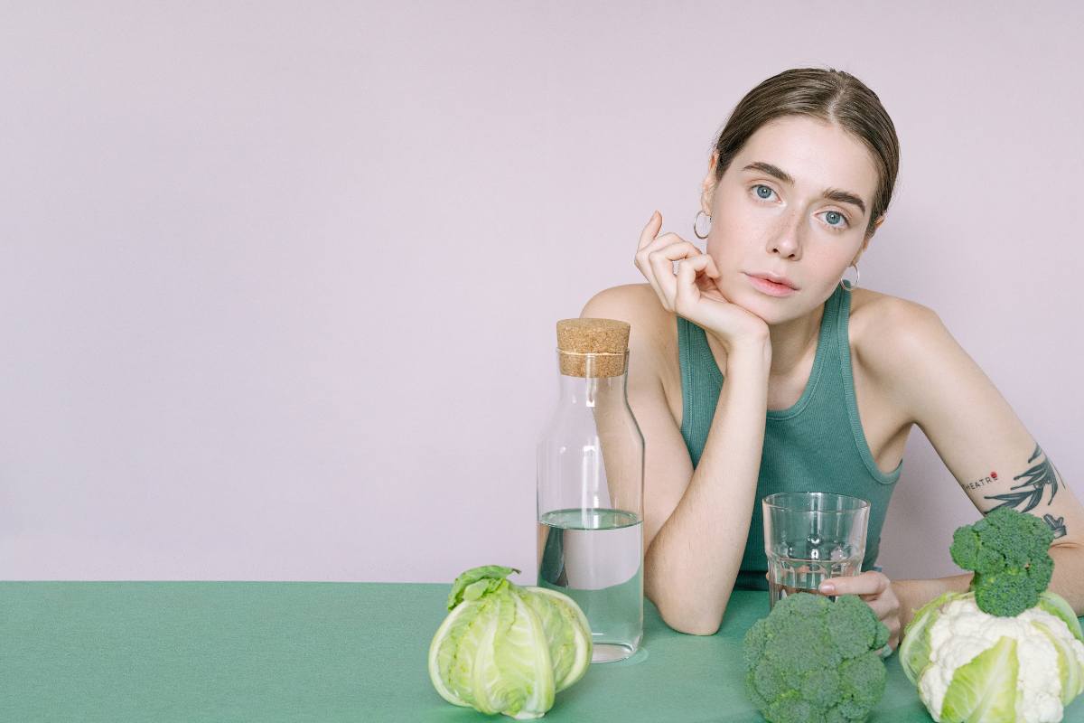 broccoli su di un tavolo con bottiglie di vetro e donna pensierosa